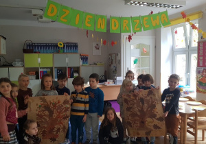 Dzieci pozują z plakatami wykonanych przez siebie drzew